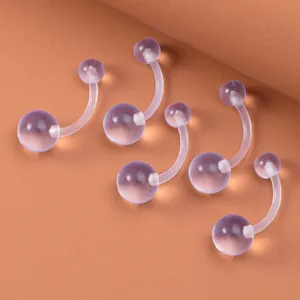 Acryl Piercing Set für Bauchnabel auf warmem Hintergrund, klare Ansicht der gebogenen Barrels.