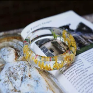 Close-up detail of a clear resin bangle bracelet featuring embedded natural yellow dried flowers.