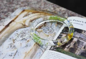 Transparent resin bangle bracelet with embedded dried green and yellow floral botanicals.