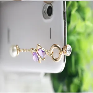 Close-up detail van de goudkleurige telefoonstofplug met parels, paarse kristallen en strass.