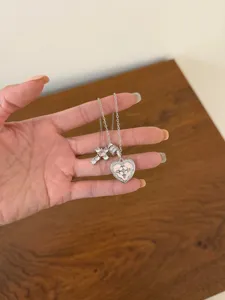 Detailed close-up of a sparkling zirconia cross and pink heart pendant necklace on a hand.