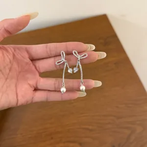 Close-up detail of sparkling rhinestone bow earrings with cute heart and pearl pendants.