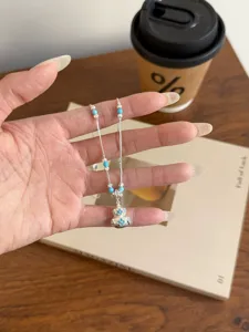 Silver tone necklace featuring blue beaded stations and a delicate clover patterned pendant.