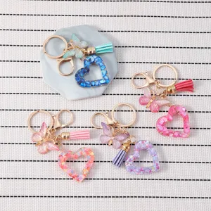 Gros plan sur le porte-clés cœur en résine colorée avec papillon et glands décoratifs.