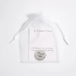 Detail view of pocket hug stainless steel token with warm message card in white organza bag.