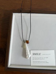 Elegante collana con ciondolo in perla di conchiglia bianca e perla marrone con barra metallica.