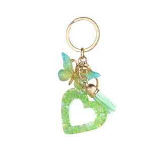 Détail de porte-clés cœur en résine pailletée verte avec breloque papillon et pompon.