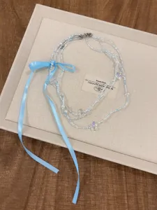 Dettaglio collana di perle delicata a tre strati con grazioso fiocco blu, gioiello di design di nicchia.