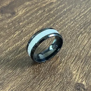 Détail de bague en acier inoxydable avec bords biseautés doubles et incrustation argentée.