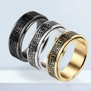 Primo piano di tre anelli spinner in metallo nero, argento e oro con motivi intagliati.