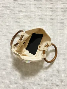 Interior detail view of beige canvas tote bag with wooden ring handles showing phone storage.