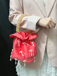 Gros plan du pendentif en perles et de la poignée perlée du sac seau rose en satin.