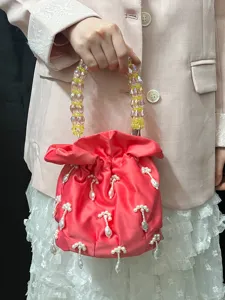 Vue détaillée du sac seau en satin rose avec poignée en perles de cristal et pendentifs.
