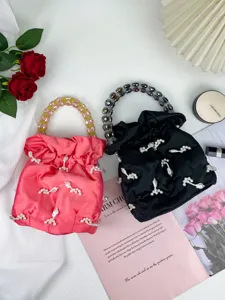 Gros plan de sacs seau en satin élégants avec poignées perlées et pendentifs de perles.