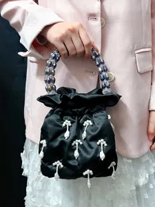 Détail en gros plan du sac seau en satin noir avec poignée perlée et pendentifs de perles.