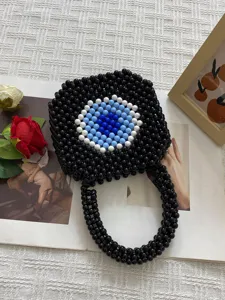 Handmade black beaded handbag featuring a striking blue evil eye pattern and rounded handle.