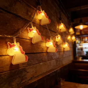 Close-up detail of cute unicorn LED string lights glowing with warm light on rustic wood wall.