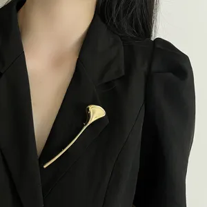 Close-up detail of smooth gold-tone alloy leaf brooch pinned on black suit lapel elegance.