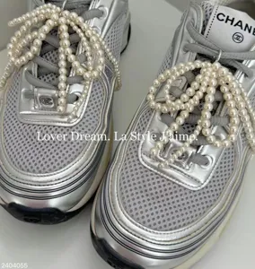 Silver sneaker upper detail with elegant pearl string bow accessories and branded tongue design.