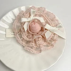 Vue détaillée de la broche fleur de rose en dentelle rose avec des nœuds de ruban blanc.