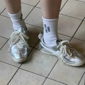 Silver metallic sneakers with pearl bow accessories and white socks, fashionable footwear.