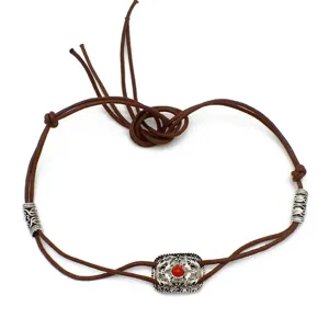 Close-up of brown leather hat band detail, featuring silver metal charm with red stone bead.