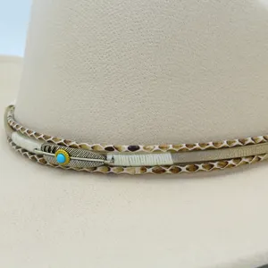 Primo piano dettaglio di cappello fedora beige con fascia intrecciata e piuma di metallo.