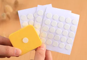 Close-up view of transparent round double-sided adhesive glue dots sheets with a yellow dispenser tool.