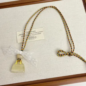Detail shot of the charming mini handbag pendant necklace featuring a delicate lace bow and colorful cord.