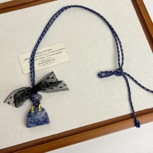 Close-up detail of a unique handbag stone pendant necklace featuring a black lace bow and cord.