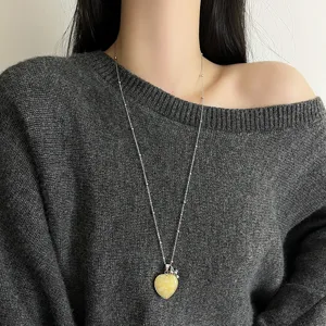Close-up detail shot of a long silver chain necklace featuring a charming yellow heart pendant.