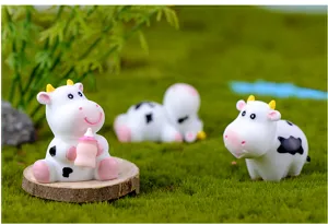 Close-up of miniature resin dairy cow figurines in a moss micro landscape, perfect for garden decor.