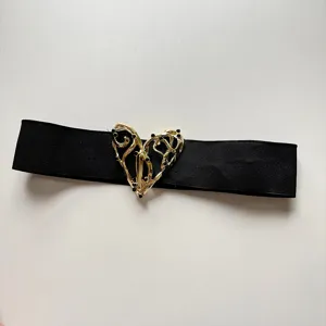 Women's black elastic waist belt with ornate hollow gold heart buckle detail accessory.