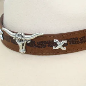 Close-up detail of western cowboy hat with brown leather band, metal bull skull and X decor.
