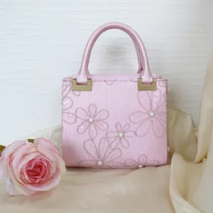 Pink embroidered handbag with pearl accents and gold hardware, elegant evening bag detail.