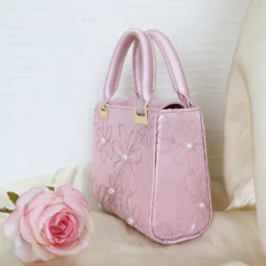 Pink satin handbag detail featuring delicate embroidered floral patterns and elegant pearl accents.