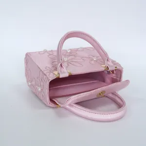 Pink embroidered satin evening handbag close-up showing floral pearls and metal hardware details.