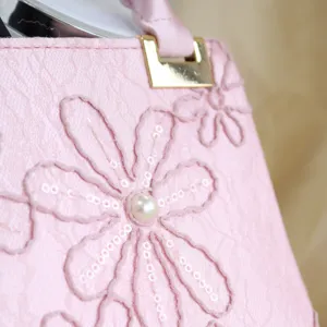 Close-up view of a pink women handbag featuring exquisite embroidered floral details and pearls.