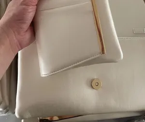 Detailed view of elegant off-white leather shoulder bag with gold metal clasp and pouch.