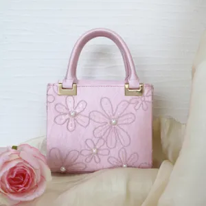 Detail shot of a delicate pink embroidered handbag featuring floral patterns and pearls.