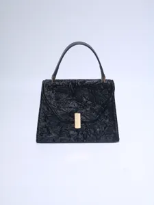 Close-up detail of black textured handbag with golden metal clasp and single handle.