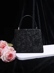 Close-up view of the elegant black textured top-handle handbag displayed with pink roses.