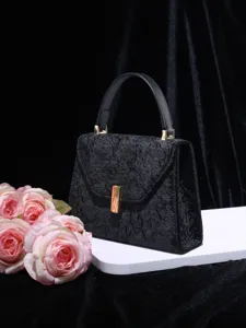 Close-up detail of black textured top-handle handbag with gold hardware and luxury design.