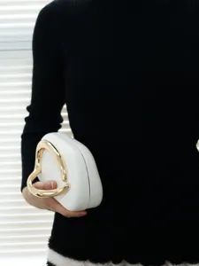 White evening bag detail showing unique gold geometric metal handle and clean leather texture.