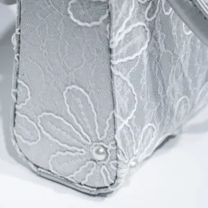 Close-up detail of silver lace embroidered women handbag with delicate white floral patterns.