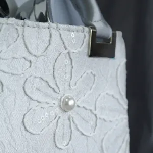 Detail view of white embroidered women evening handbag with pearl and silver hardware accent.
