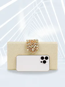 Gold glitter evening clutch bag detail showing rhinestone clasp and size reference phone.