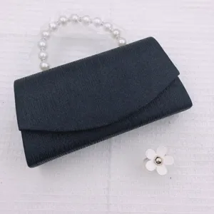 Detail view of black evening clutch bag featuring elegant pearl handle and sleek fabric texture.