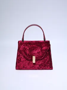 Burgundy velvet textured handbag detail showcasing elegant gold metal clasp and top handle.