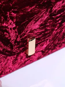 Close-up detail of luxurious dark red velvet handbag texture with a shiny gold metal clasp.